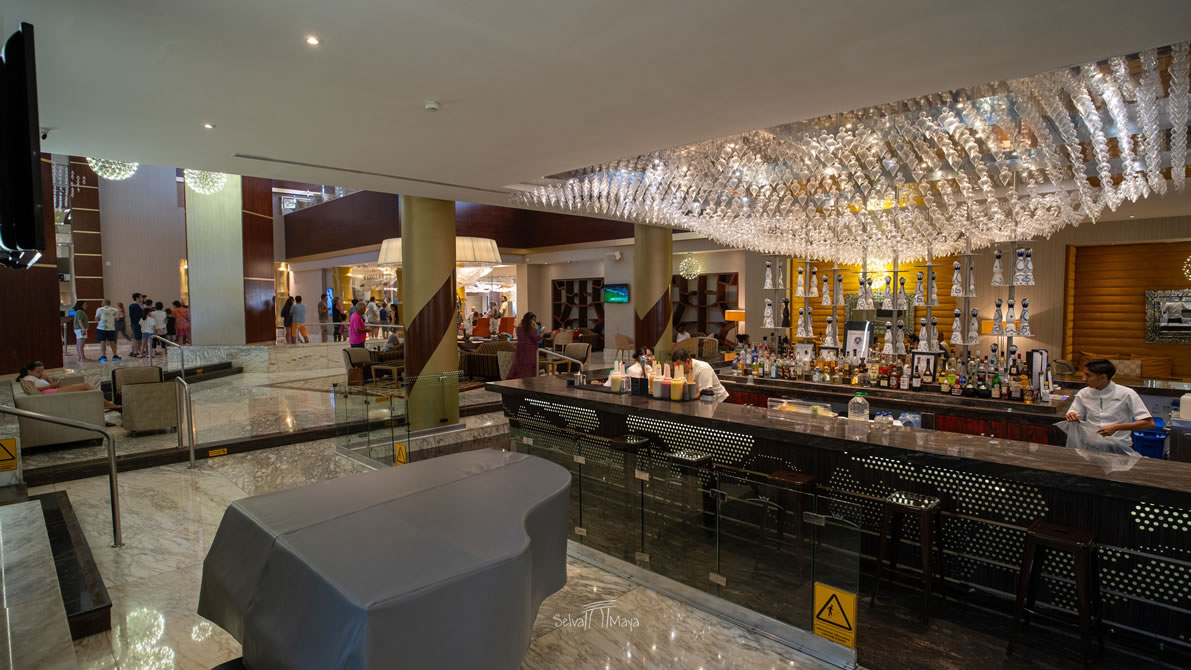 Lobby bar de Nizuc con barra iluminada, bartenders y candelabro de cristal