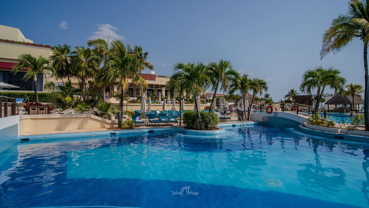 Alberca curva de varios niveles en Moon Palace Cancún, con puente peatonal e isletas de palmeras