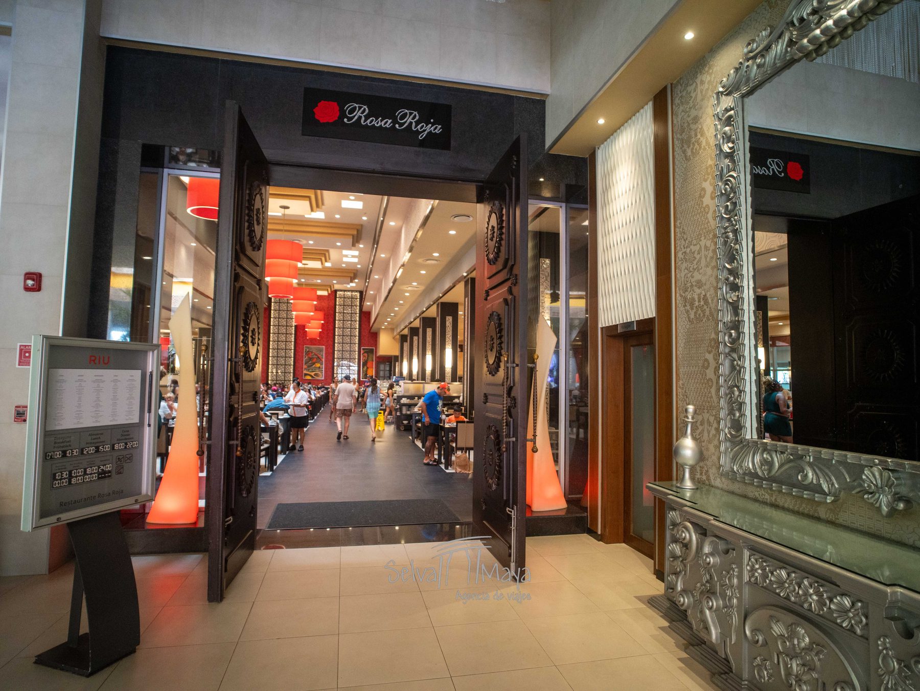 Entrada del buffet Rosa Roja del Riu Tequila con lámparas rojas y el atril de horarios