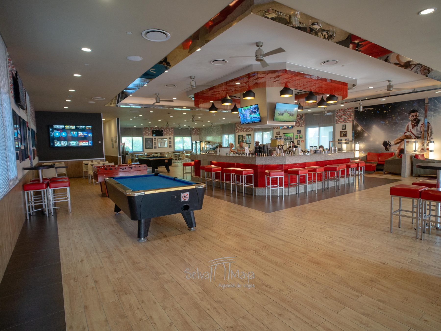 Sport bar del Riu Tequila con barra, taburetes rojos, mesa de billar y pantallas de deportes