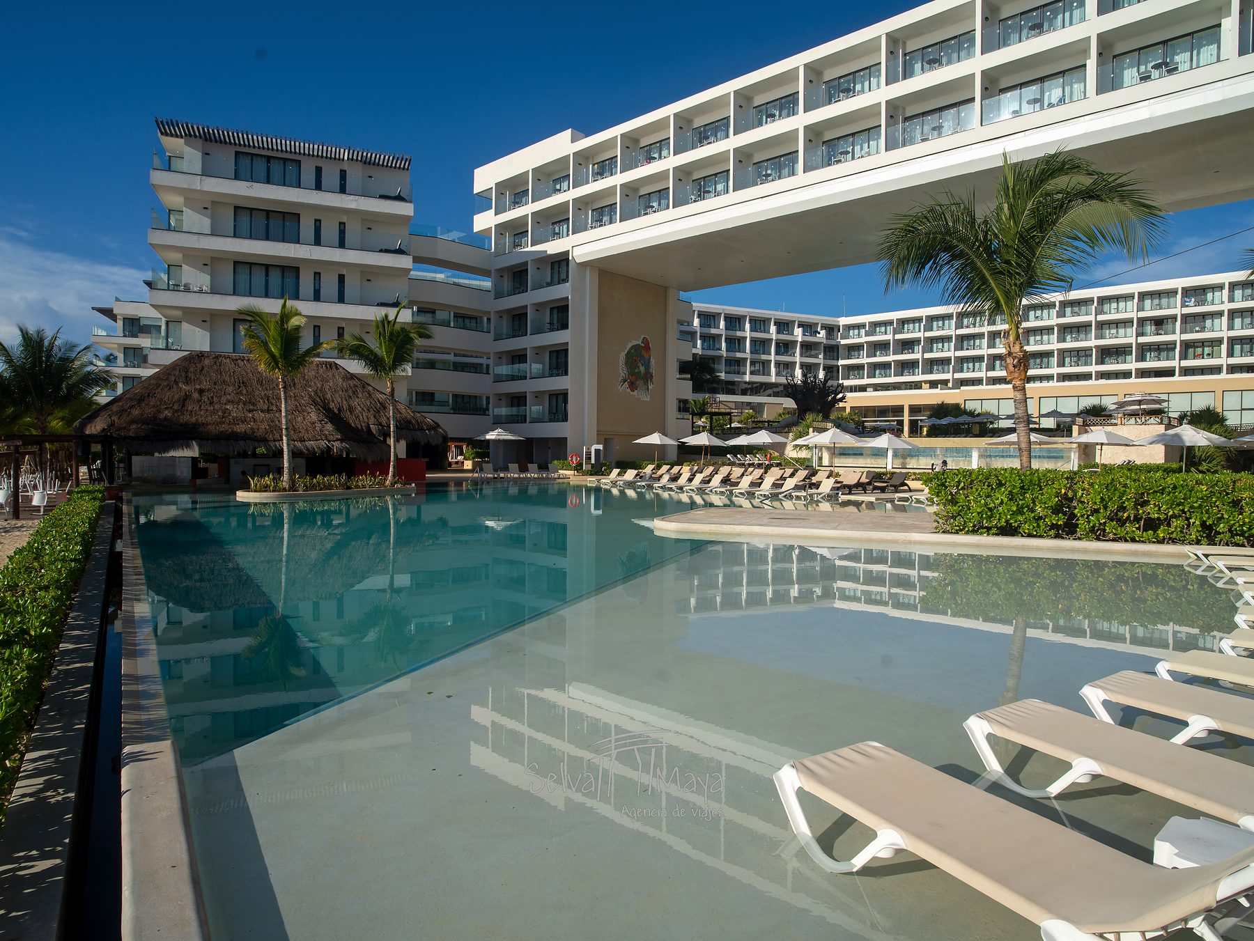 Alberca con palapa y edificio de habitaciones en Sensira Resort Riviera Maya