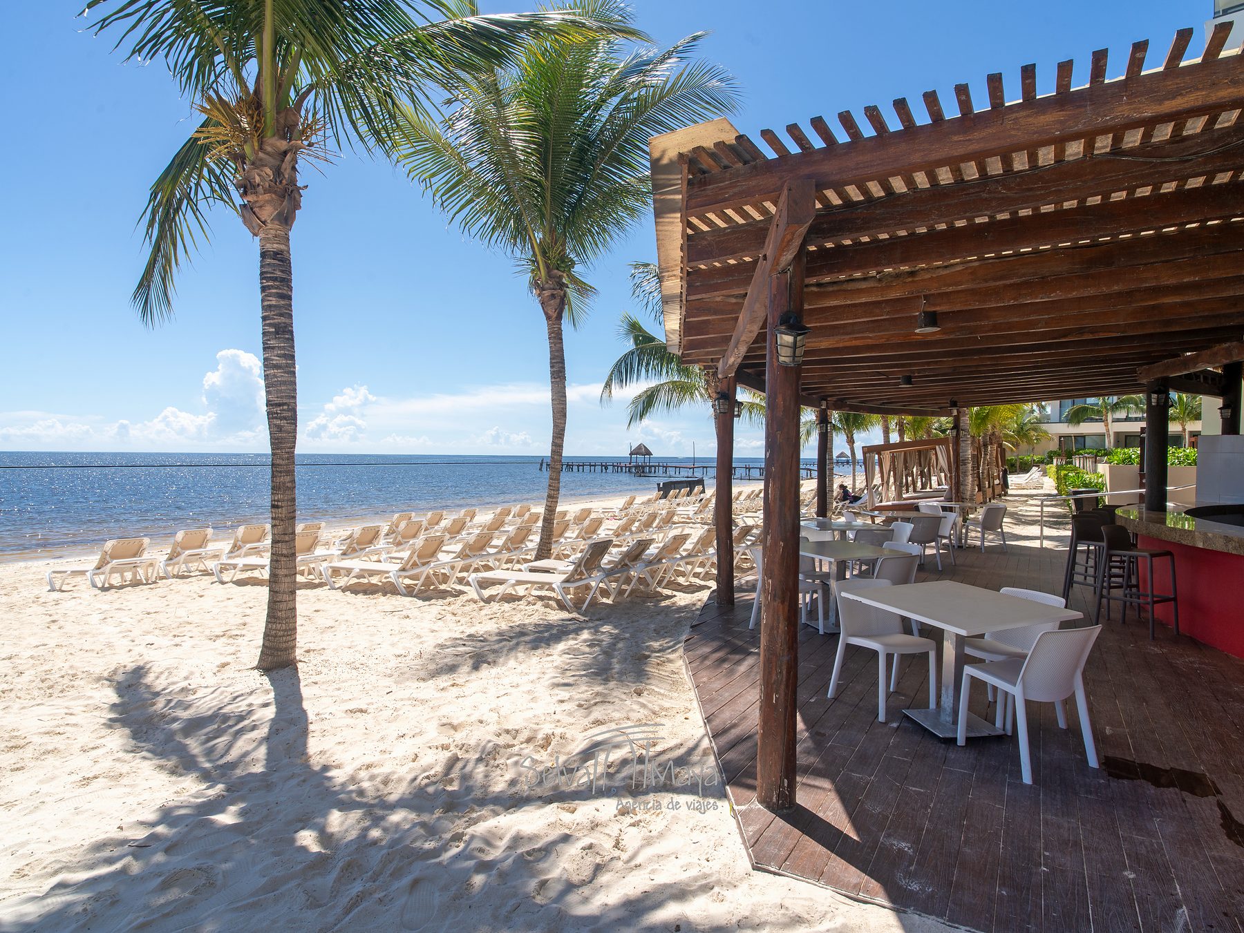 Terraza de madera y barra junto a la playa en Sensira Resort Riviera Maya
